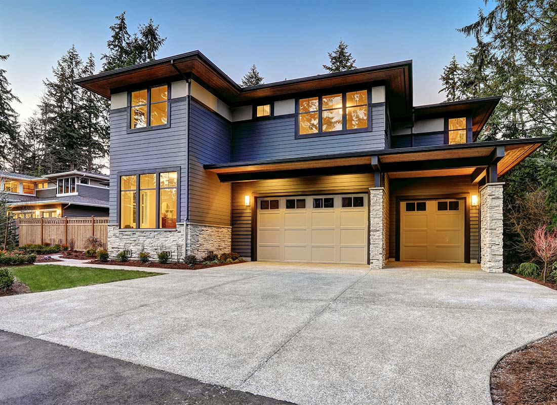 Home Insurance - Exterior View of a Modern Two Story Home with a Two Car Garage and a Concrete Driveway with Beautiful Landscaping in the Evening