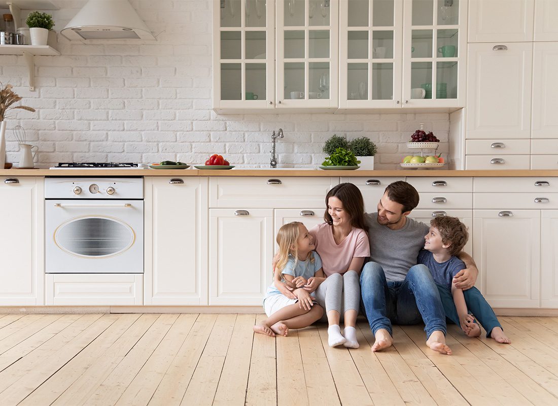Personal Insurance - Portrait of a Young Family with a Son and Daughter Spending Time Together at Home While Sitting on the Floor in Their Modern Kitchen