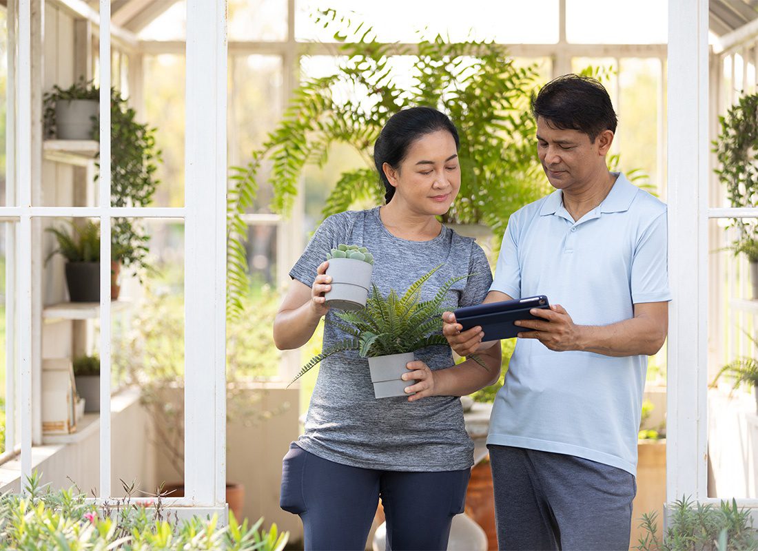 Service Center - Portrait of a Middle Aged Married Couple Standing Inside a Glass Greenhouse Full of Plants While Looking at a Tablet